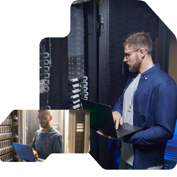 A man in a server room, intently focused on his laptop, stands beside tall racks with glowing equipment