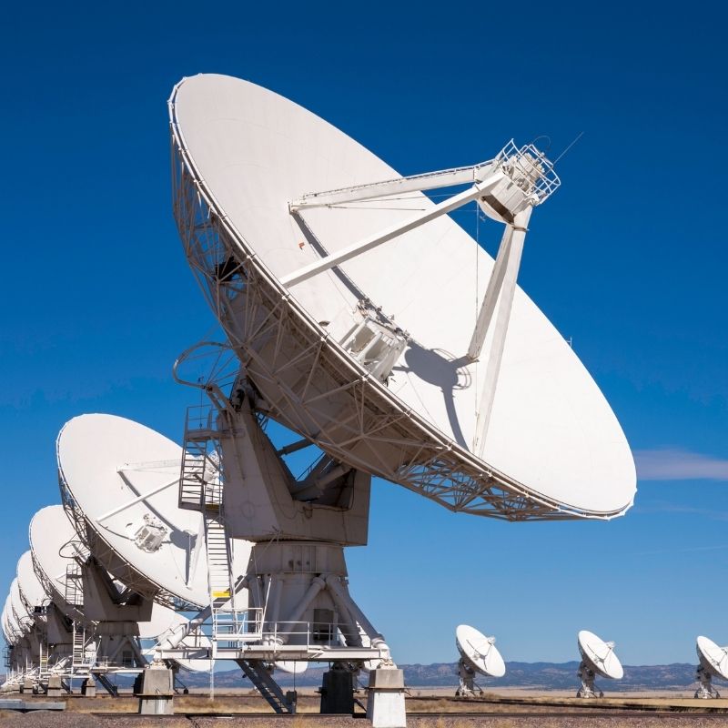 A row of large white satellite dishes aimed at the sky against a clear blue backdrop