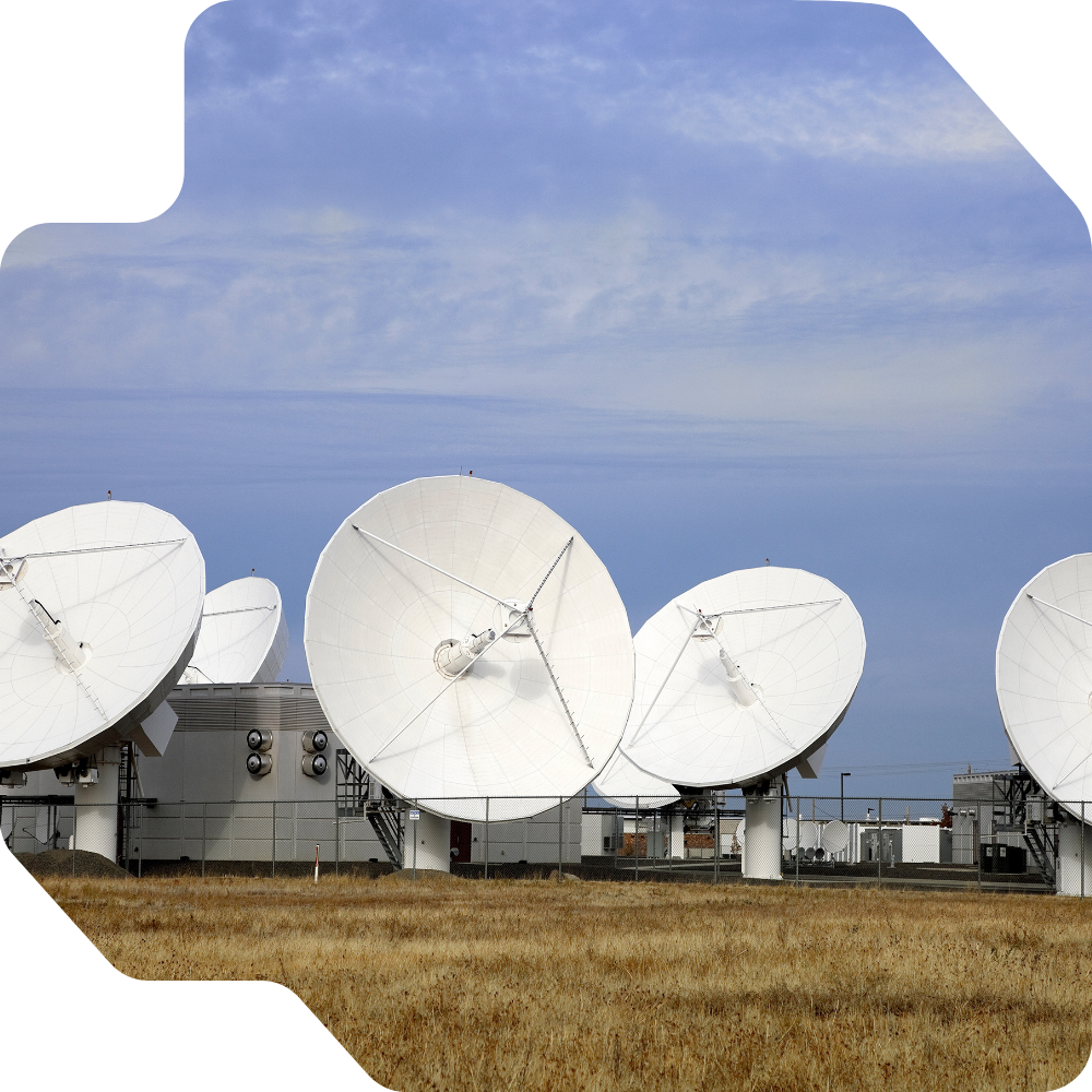 Array of large white satellite dishes in a grassy field, pointing skyward under a clear blue sky
