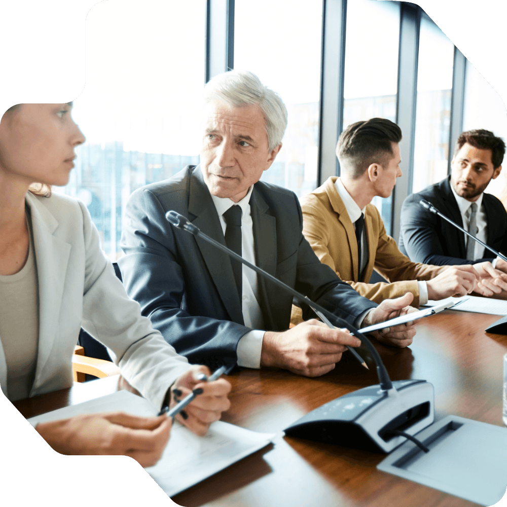 Four professionals in a modern conference room sit at a table with microphones_compressed