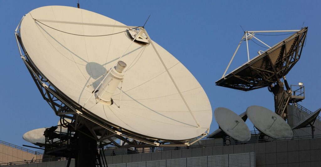 Two satellite dishes mounted on the roof of a building against a clear blue sky.