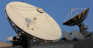 Two satellite dishes mounted on the roof of a building against a clear blue sky.